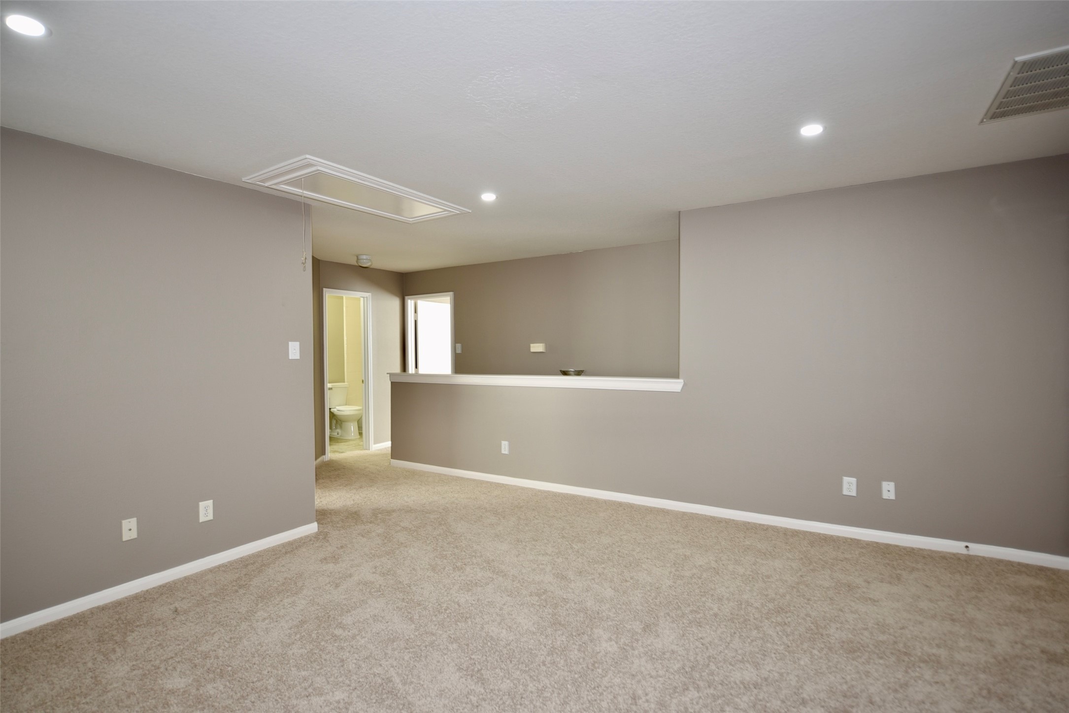 9611 Babbling Spring Court Tomball, TX 77375 - Photo 19 of 31 This room features neutral walls and carpeting, recessed lighting, and an open layout with a partial wall dividing spaces. A door leads to a bathroom, making it versatile for various uses.