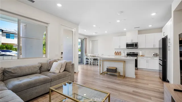 a living room with stainless steel appliances kitchen island granite countertop a refrigerator a stove a sink and a dining table with wooden floor