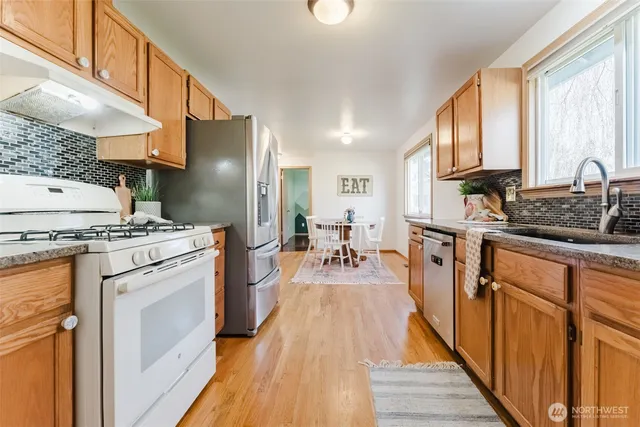 a kitchen with kitchen island granite countertop a stove a sink dishwasher and a refrigerator with wooden floor