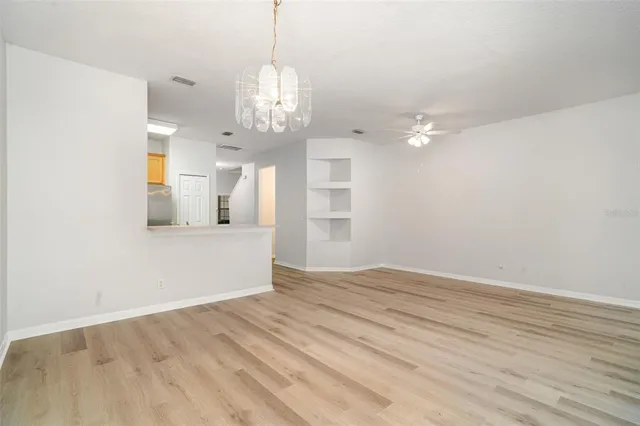 a view of empty room with wooden floor and kitchen view