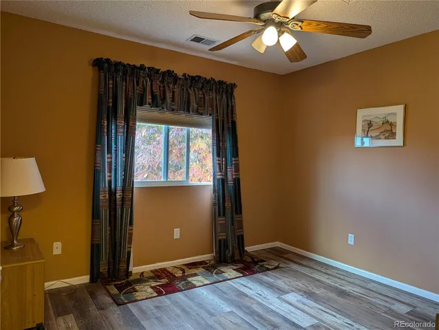 an empty room with wooden floor chandelier fan and windows