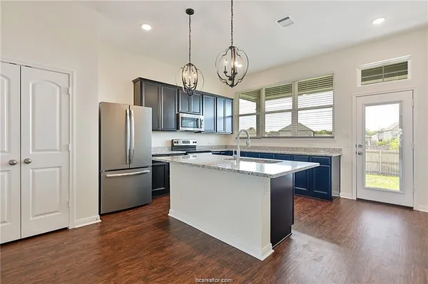 a kitchen with stainless steel appliances granite countertop a refrigerator a stove a sink and a center island with wooden floor