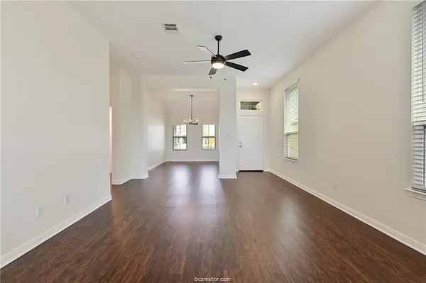 an empty room with wooden floor ceiling fan and windows