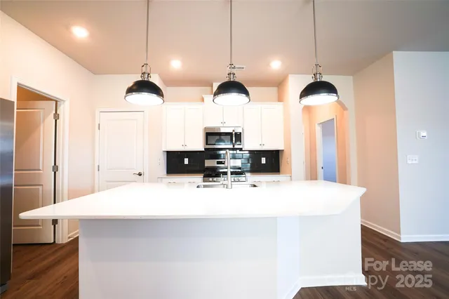 a kitchen with stainless steel appliances kitchen island a white cabinets and a wooden floor