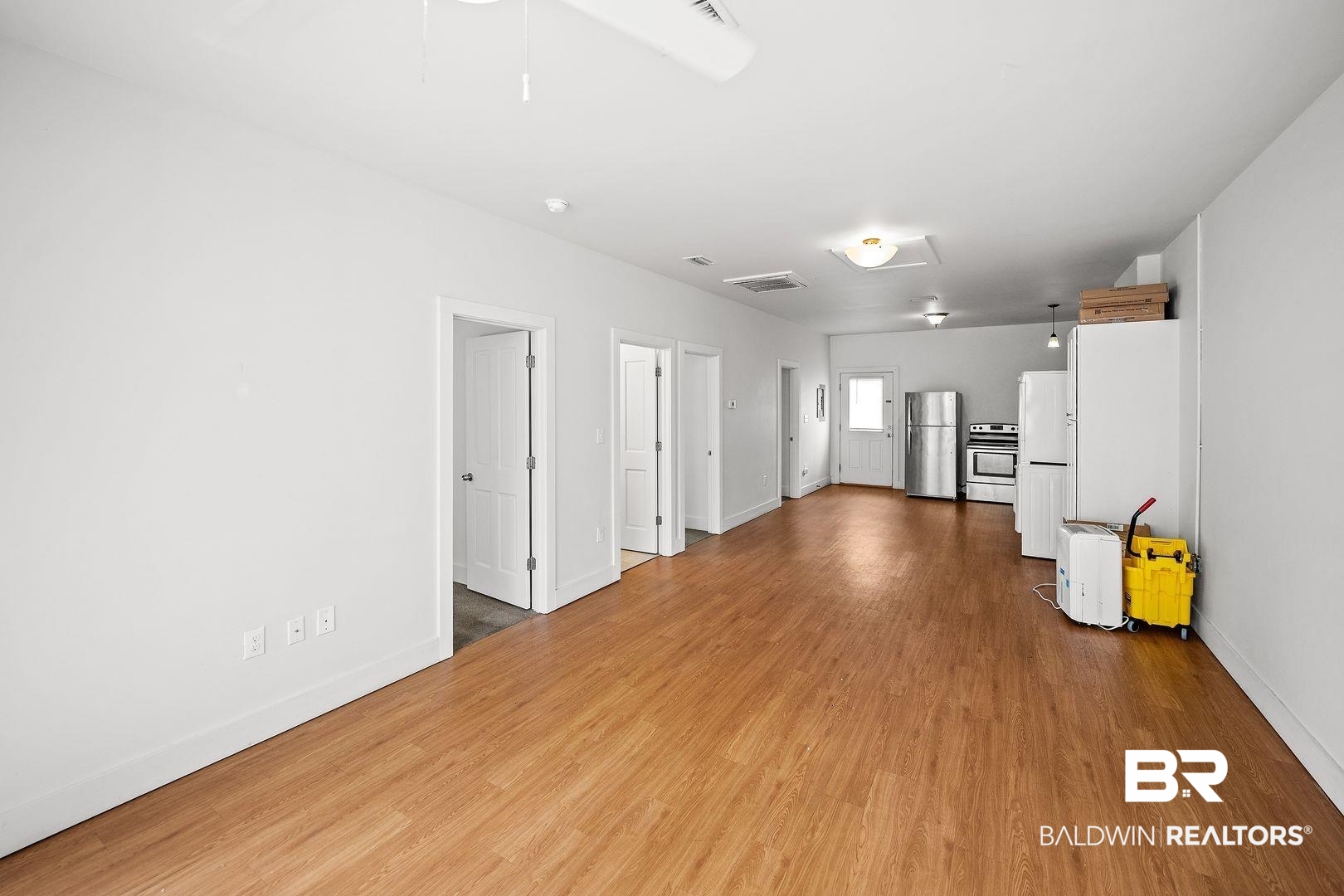 635 East Azalea Avenue Foley, AL 36535 - Photo 13 of 18 Open-concept living space featuring wood-finish flooring, white walls, multiple doorways, and a kitchen area equipped with a stainless steel refrigerator and range