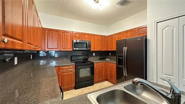 a kitchen with stainless steel appliances granite countertop a refrigerator a stove and a sink with wooden cabinets