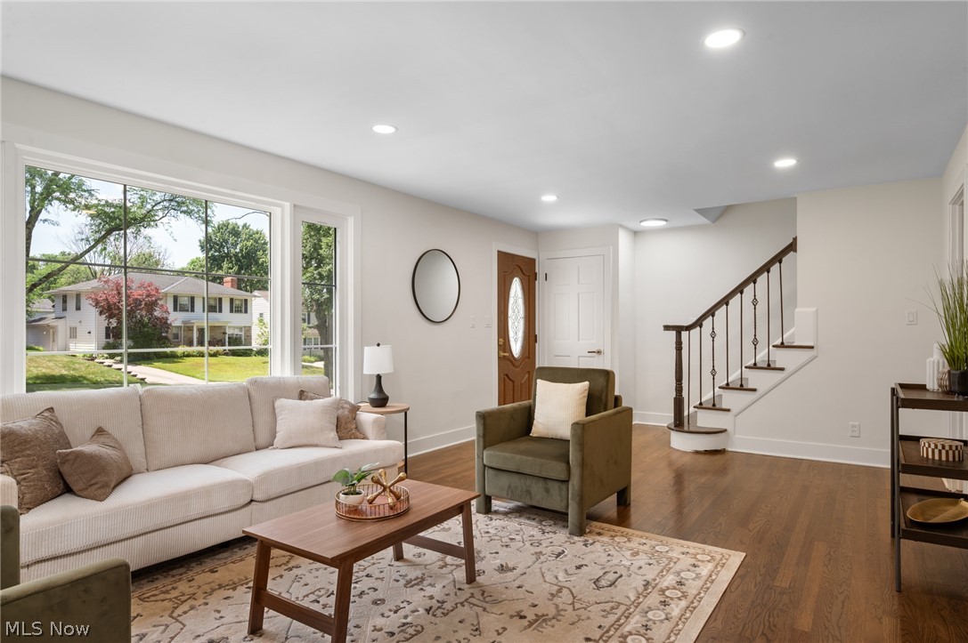22625 Rye Road Shaker Heights, OH 44122 - Photo 6 of 38 Spacious living area featuring large picture windows, recessed lighting, rich wood-finish flooring, a classic staircase with dark wood handrails and metal balusters, and a panel-style entry door