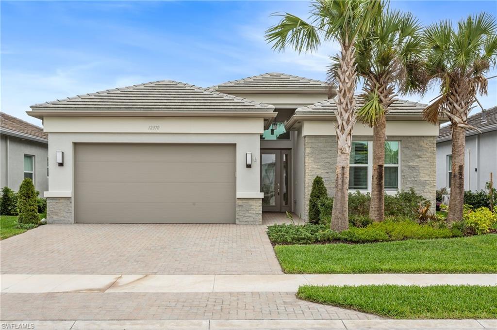 12370 Purple Ficus Way Naples, FL 34120 - Photo 35 of 50 Prairie-style house featuring stone siding, an attached garage, decorative driveway, a front lawn, and stucco siding