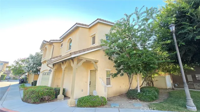a white house with a large tree and plants next to it