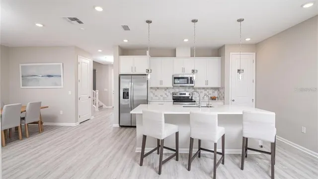 a large kitchen with stainless steel appliances kitchen island granite countertop a dining table chairs and white cabinets