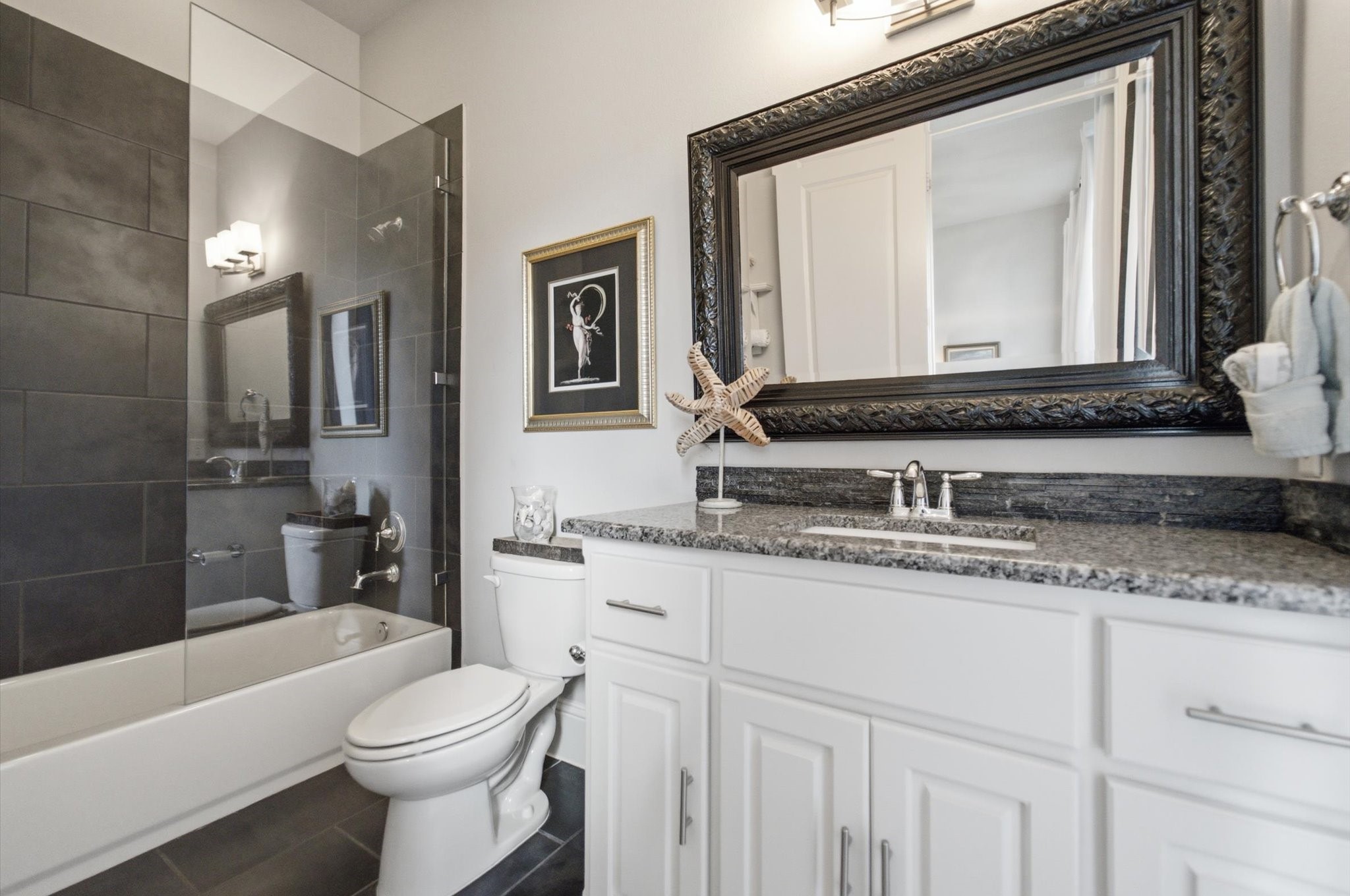 23722 Thortons Park Lane Spring, TX 77389 - Photo 20 of 48 This bathroom features modern amenities with a sleek design. It includes a glass-enclosed bathtub with dark tile accents, a granite countertop, and white cabinetry. The large decorative mirror and soft lighting enhance the space's elegance.
