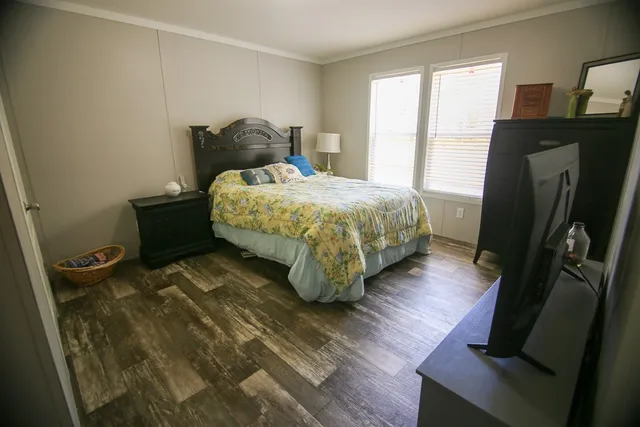 a bedroom with a bed wooden floor and a flat tv screen on the dresser