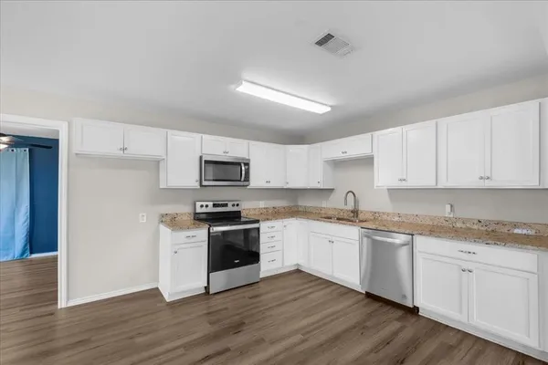 a kitchen with stainless steel appliances granite countertop a stove top oven a sink and white cabinets