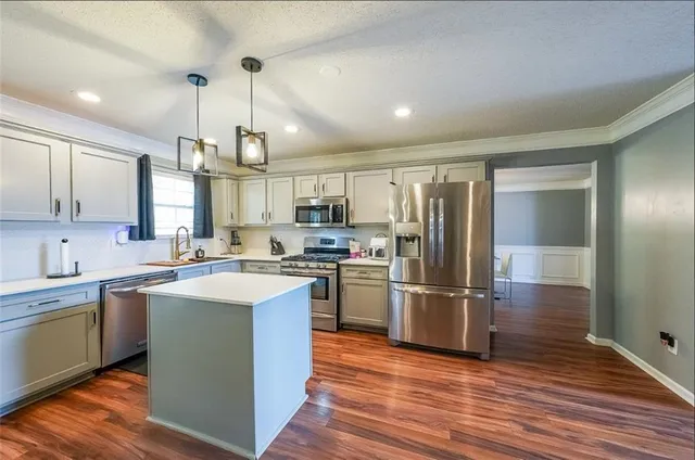 a kitchen with stainless steel appliances granite countertop a refrigerator a sink dishwasher a stove and white countertops with wooden floor