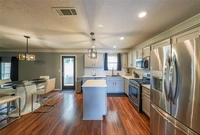 a kitchen with stainless steel appliances granite countertop a refrigerator a stove top oven a dining table and chairs with wooden floor