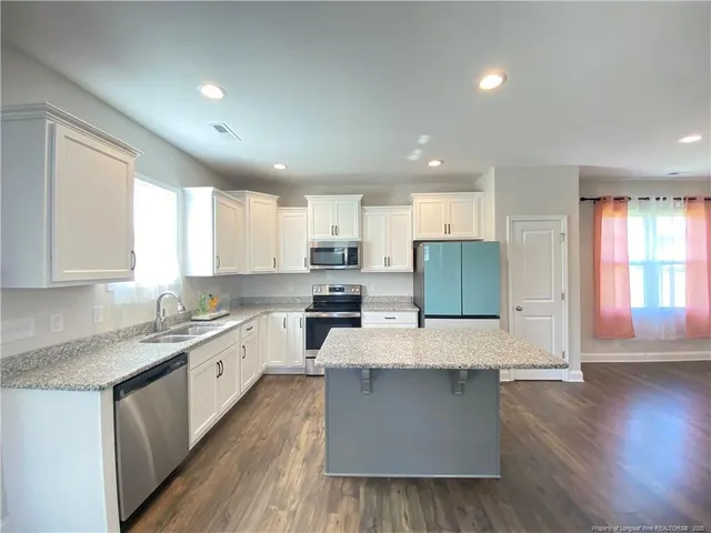 a large kitchen with stainless steel appliances kitchen island granite countertop a stove a sink a refrigerator and white cabinets with wooden floor