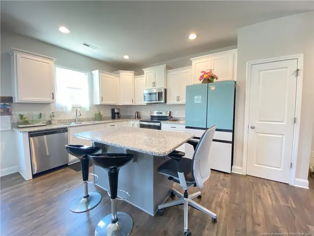 a kitchen with granite countertop a table chairs a sink dishwasher refrigerator and cabinets
