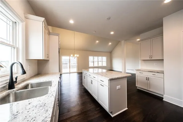 a kitchen with stainless steel appliances granite countertop a stove a sink a refrigerator and white cabinets with wooden floor