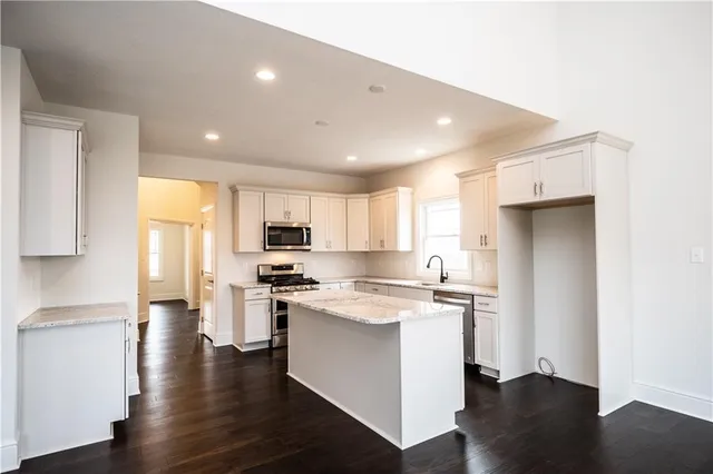 a kitchen with stainless steel appliances granite countertop a refrigerator a sink dishwasher a stove and white countertops with wooden floor