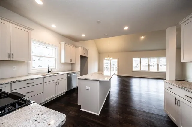 a kitchen with stainless steel appliances kitchen island granite countertop a stove a sink and white cabinets with wooden floor