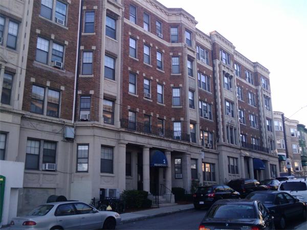 a front view of a building with lot of cars and trees