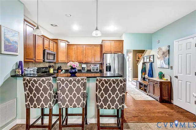 a kitchen with stainless steel appliances granite countertop a refrigerator a stove a sink dishwasher a dining table and chairs with wooden floor