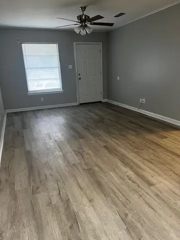 an empty room with wooden floor chandelier fan and windows