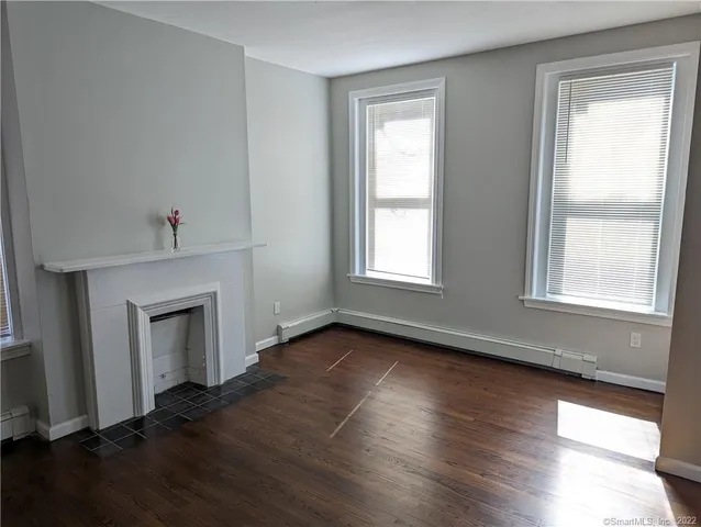 an empty room with wooden floor fireplace and windows