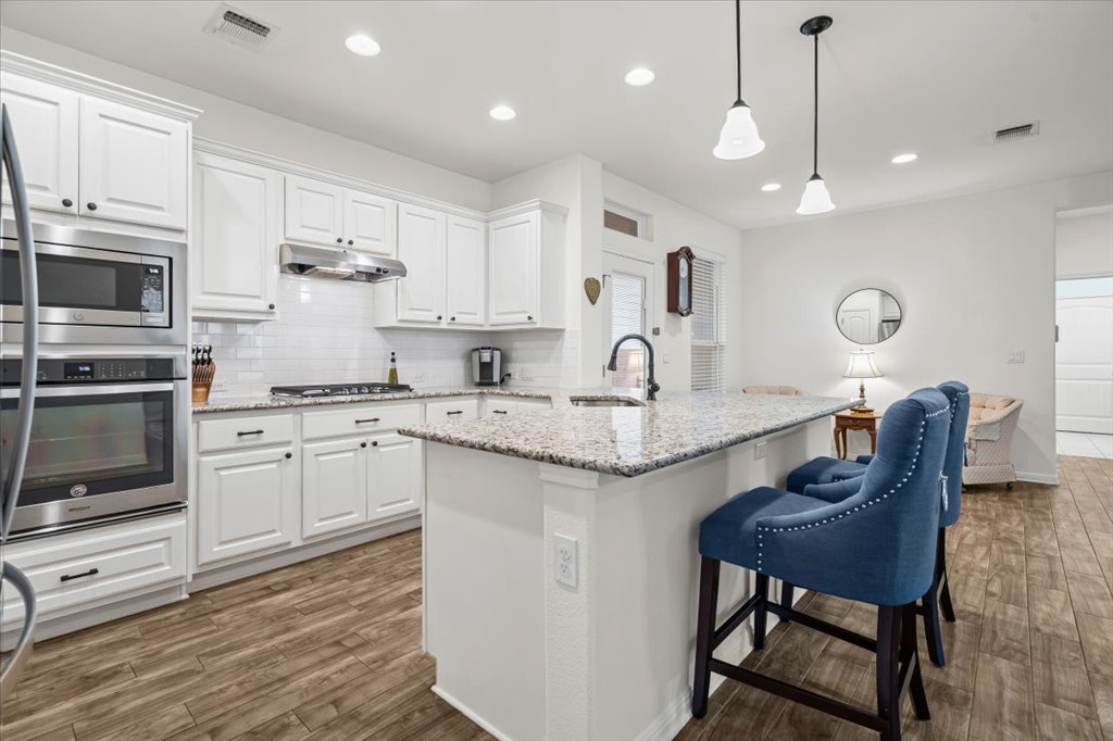 5912 Corrine Lane Austin, TX 78747 - Photo 6 of 27 Gourmet Style Kitchen featuring white cabinets, pendant lighting, stainless steel appliances, and light stone counters