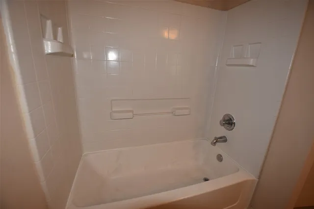 an empty room with chandelier fan and kitchen view