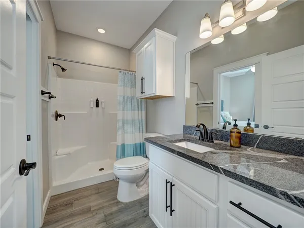 a bathroom with a granite countertop sink a toilet a mirror and shower