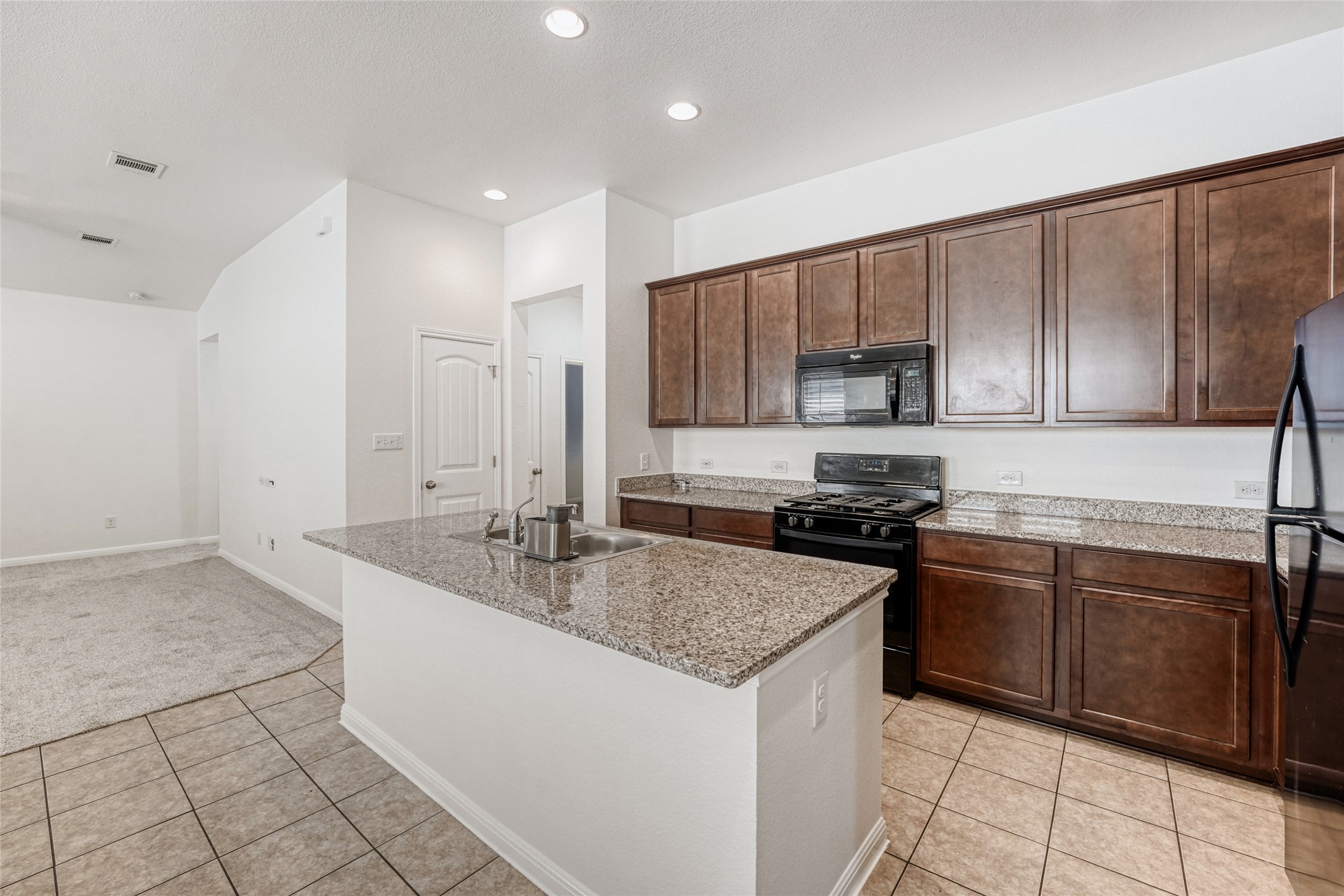410 Anacua Loop, Unit 30 Manchaca, TX 78652 - Photo 11 of 33 Kitchen featuring black appliances, a center island with sink, light tile patterned floors, dark wood finish cabinets, and light stone counters