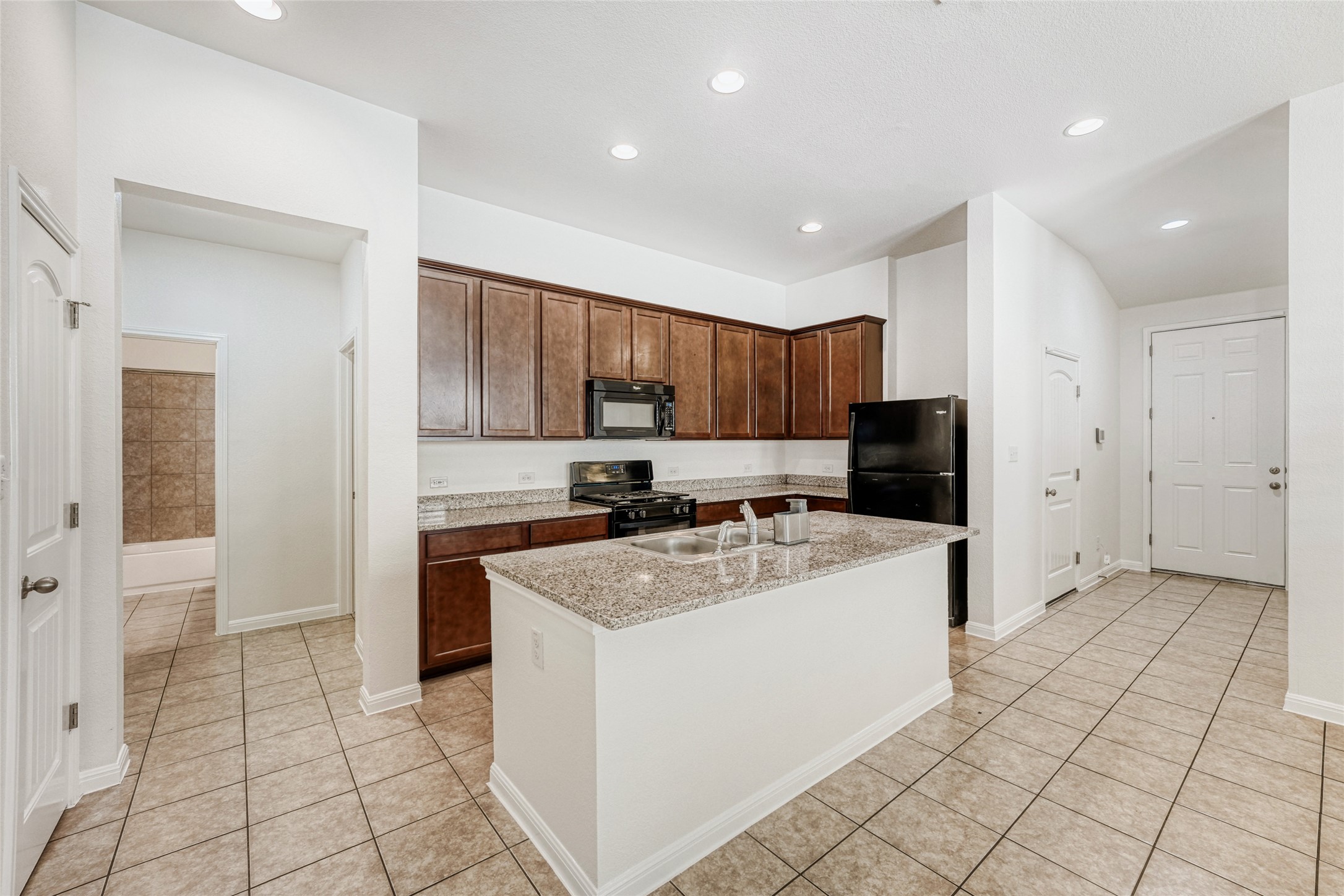 410 Anacua Loop, Unit 30 Manchaca, TX 78652 - Photo 13 of 33 Kitchen with light stone counters, black appliances, a kitchen island with sink, light tile patterned floors, and dark wood finish cabinets