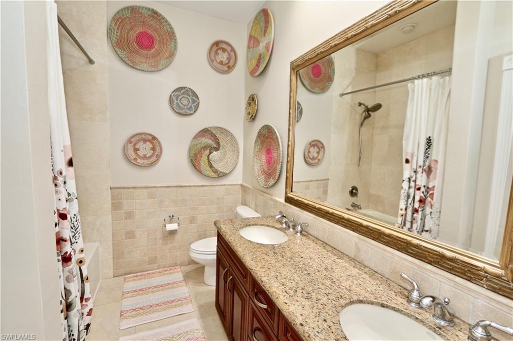 2855 Coach House Way Naples, FL 34105 - Photo 26 of 42 Full bath featuring double vanity, shower / tub combo, tile walls, a wainscoted wall, and light tile patterned flooring