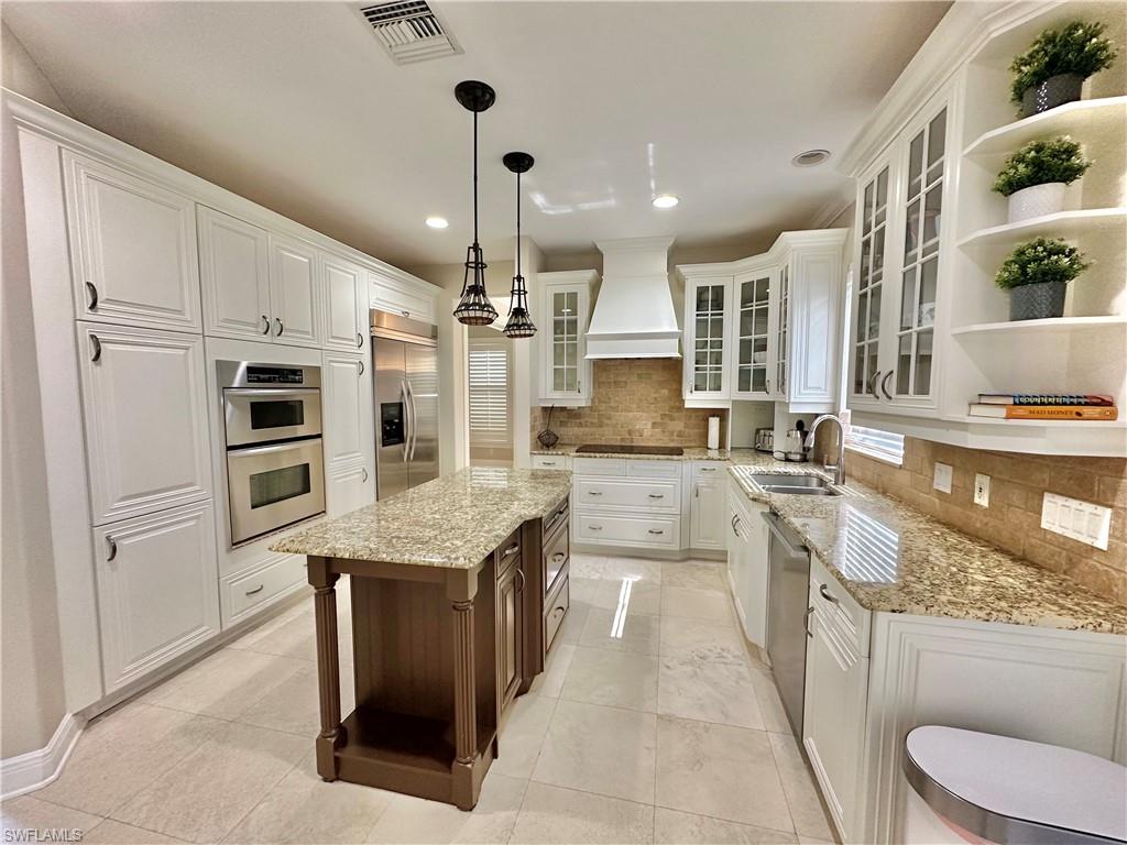 2855 Coach House Way Naples, FL 34105 - Photo 5 of 42 Dual tone kitchen with open shelves, glass insert cabinets, light stone countertops, decorative light fixtures, and two tone color scheme