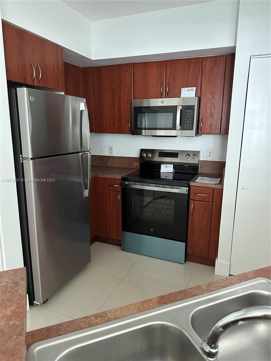 9201 Collins Avenue, Unit 524 Surfside, FL 33154 - Photo 6 of 20 a kitchen with wooden cabinets a sink and stainless steel appliances