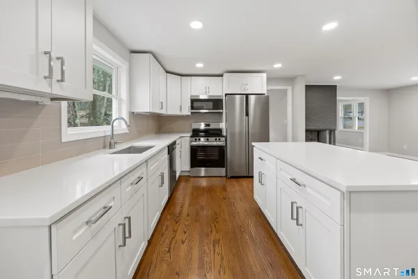 a large white kitchen with kitchen island a sink a center island stainless steel appliances and a window