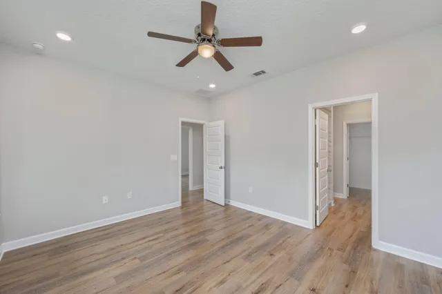 an empty room with wooden floor fan and windows
