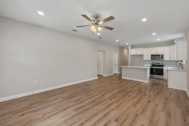 a view of an empty room with wooden floor and a ceiling fan