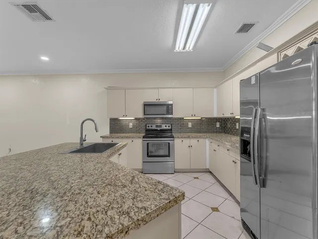 a large kitchen with granite countertop a sink white cabinets and stainless steel appliances