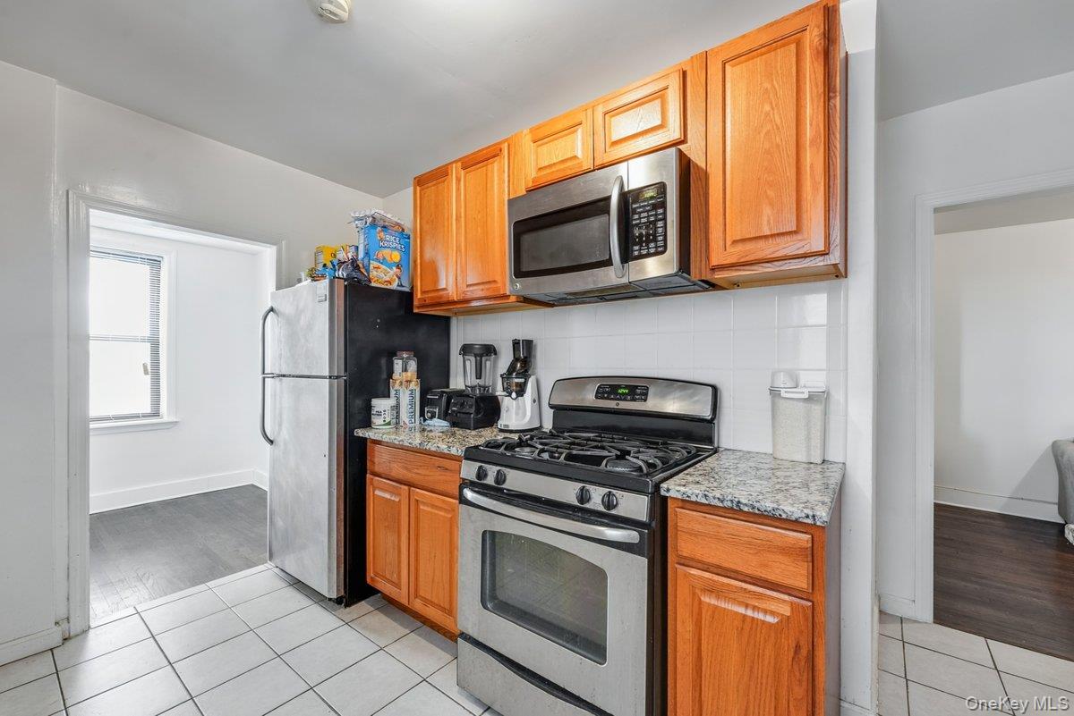 3840 Greystone Avenue, Unit 5O Bronx, NY 10463 - Photo 5 of 7 Kitchen featuring stainless steel appliances, light tile patterned flooring, decorative backsplash, light stone counters, and brown cabinets