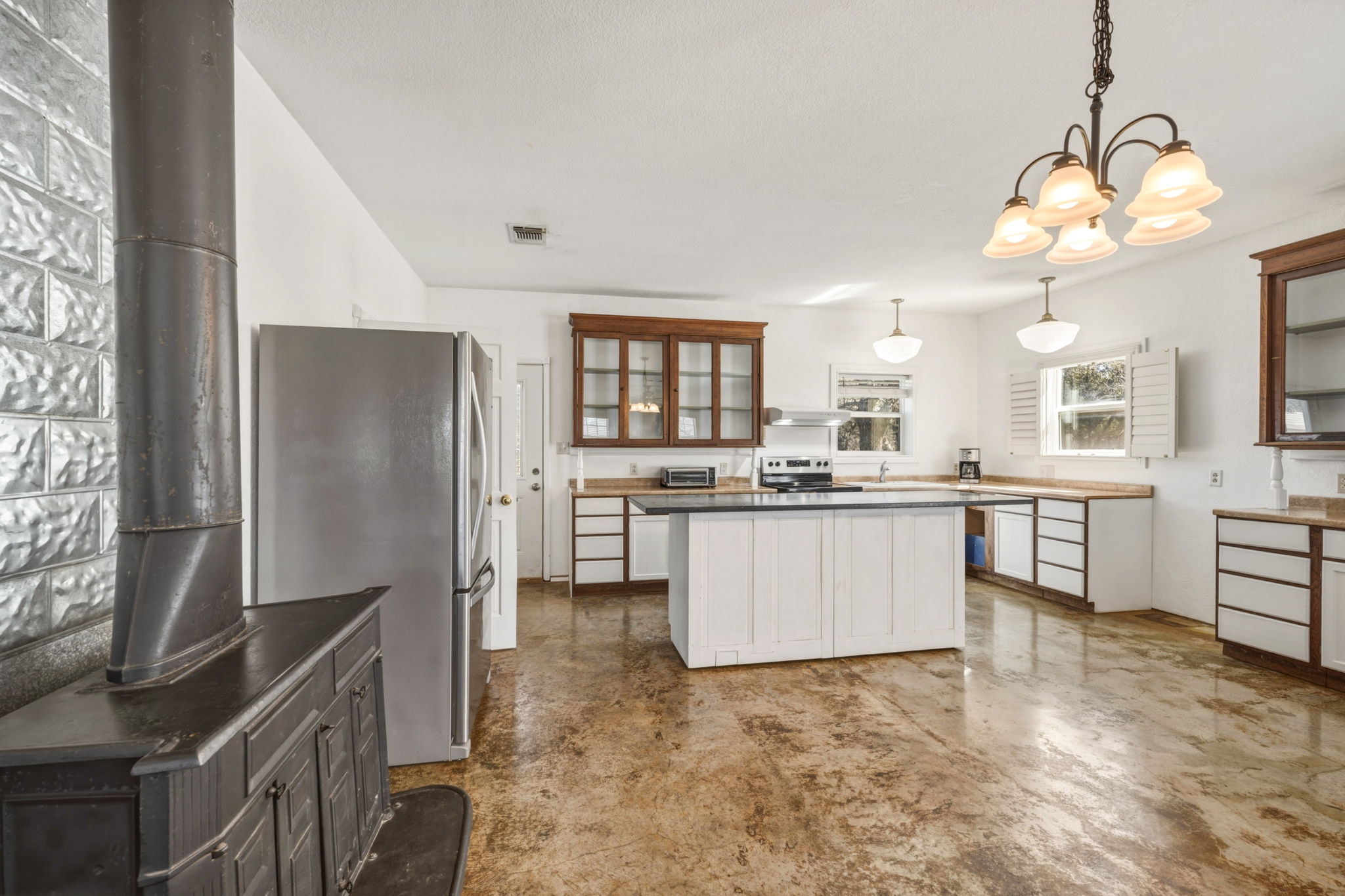 1301 Altwein Road Blanco, TX 78606 - Photo 14 of 40 Dual tone kitchen with stainless steel appliances, concrete flooring, a wood stove, hanging lights, and glass insert cabinets
