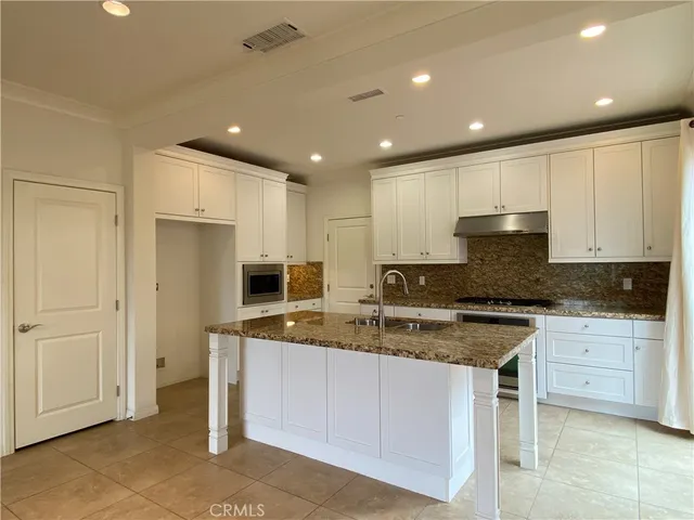 a large kitchen with stainless steel appliances granite countertop a stove a sink a refrigerator and white cabinets