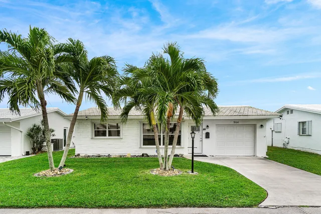 a front view of a house with a yard and palm trees