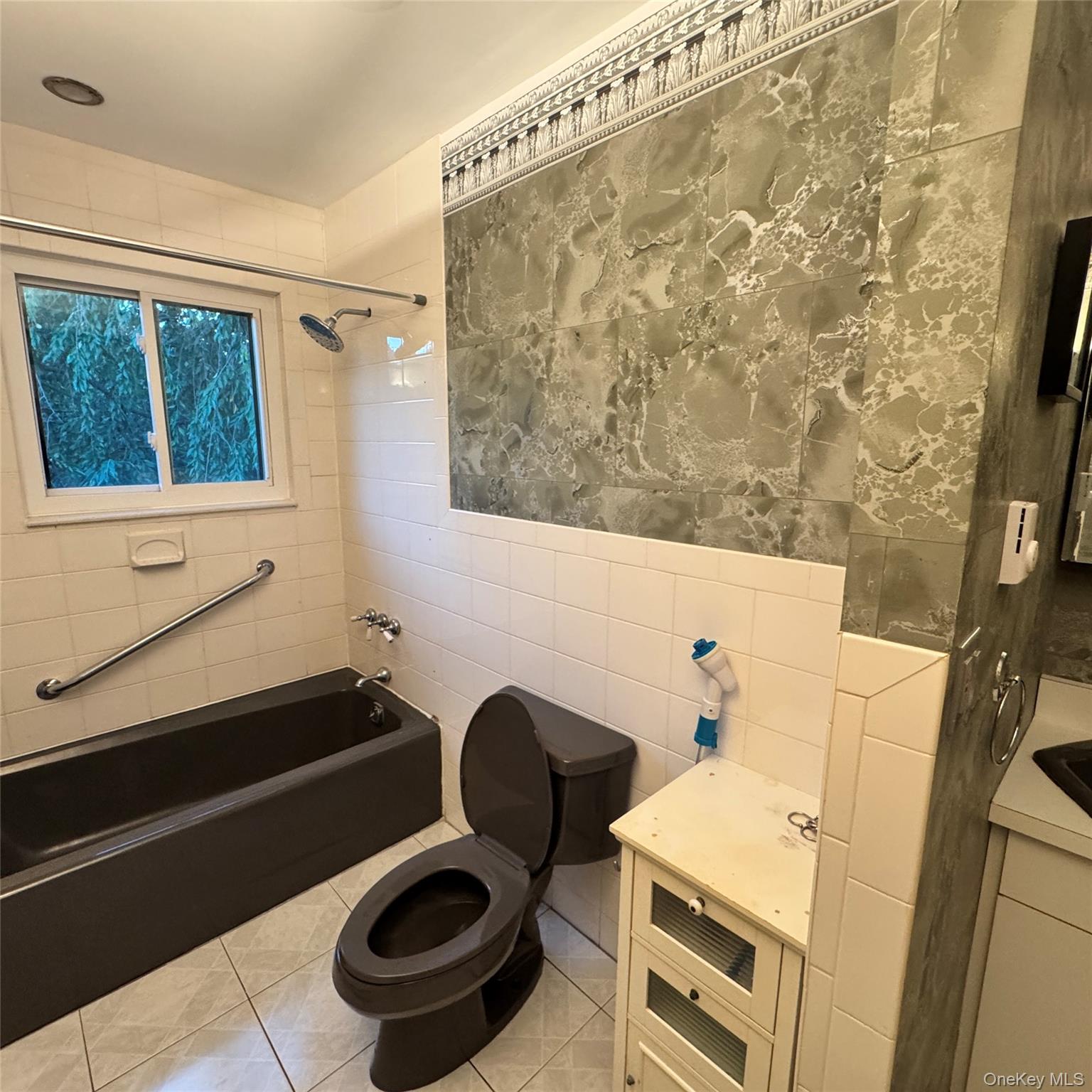 67 Steele Road New Windsor, NY 12553 - Photo 28 of 34 Full-size bathtub with grab bar, white ceramic wall tile, window with opaque glass, decorative wall paneling, and ceramic tile flooring