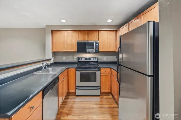 a kitchen with stainless steel appliances granite countertop a refrigerator a stove and a sink with wooden floor