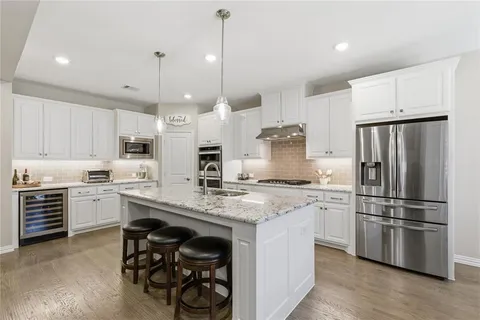 a kitchen with stainless steel appliances granite countertop a stove a sink a refrigerator and white cabinets with wooden floor