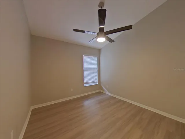 an empty room with wooden floor fan and windows