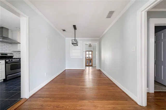 a view of an empty room with wooden floor and a kitchen