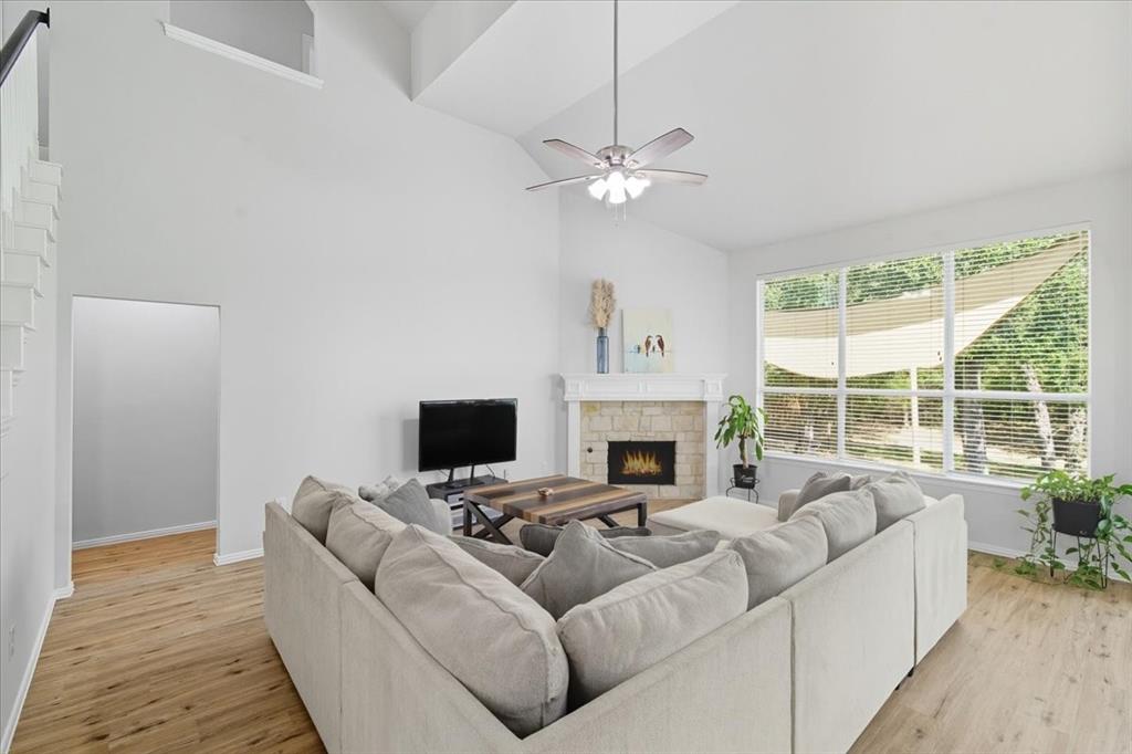 409 Springtree Road Lake Dallas, TX 75065 - Photo 10 of 40 Vaulted ceiling, wood-finish flooring, stone-clad fireplace, large picture windows, and a ceiling fan with integrated lighting